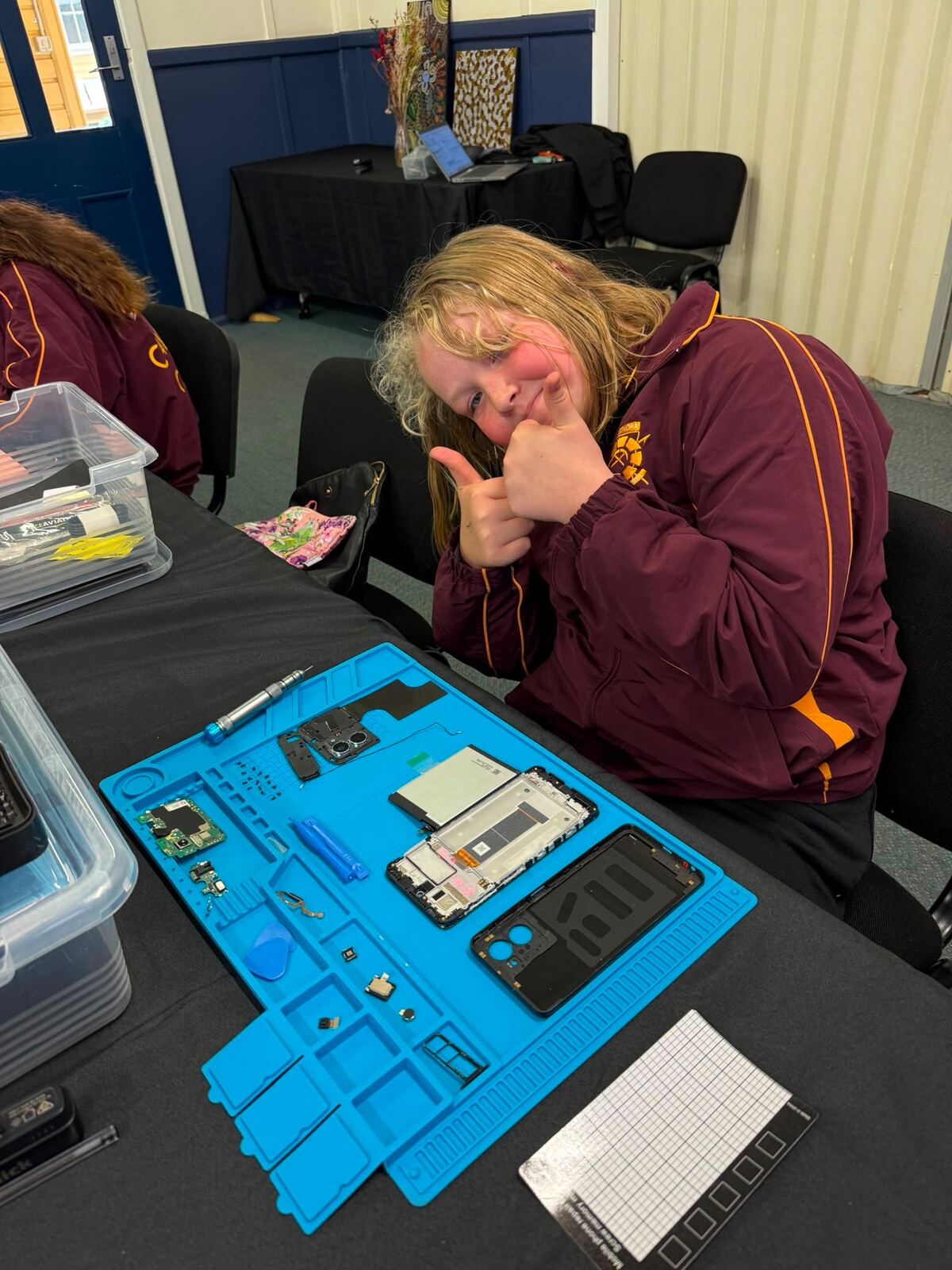 A Leonora student giving a thumbs up over a dismantled mobile phone on a repair mat