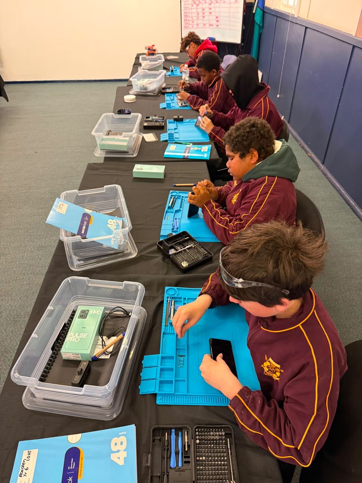Leonora students working on phone repairs at benches with tool kits and repair mats