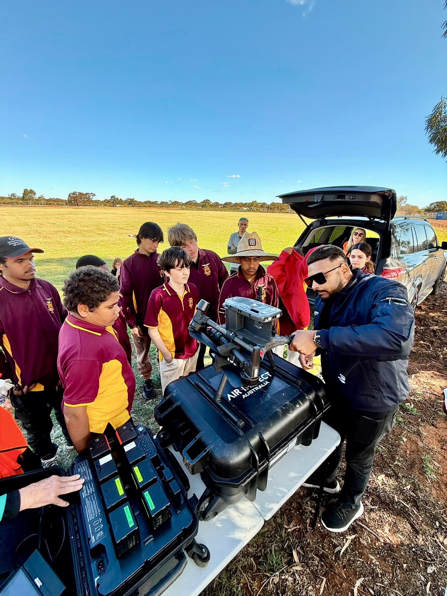 An instructor demonstrating drone equipment to students during outdoor training