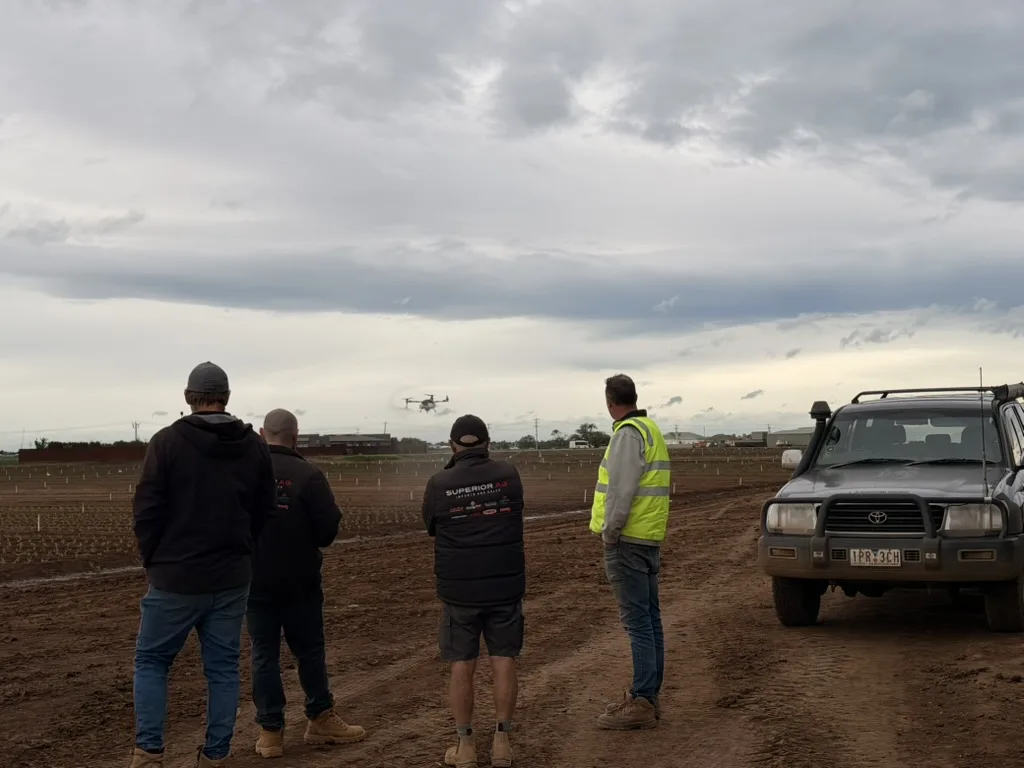 A group observing an agricultural drone flight over a planted field